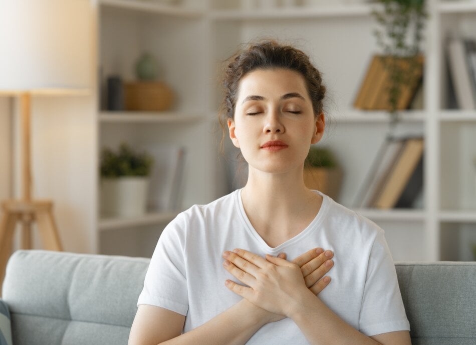 Woman sitting with hands across heart and eyes closed canva 950x690 1